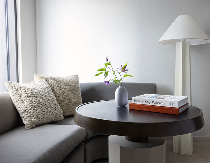 pillows on gray sofa, table with books and standing lamp